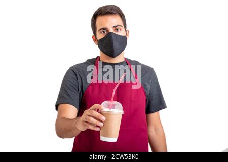 Caffè da andare al bar Coronavirus Days Concept. Il barista indossa una maschera protettiva per il viso che tiene isolato il bicchiere di carta da asporto su sfondo bianco. Foto Stock