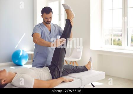 Giovane medico che esamina la gamba del giovane uomo per assegnare il diritto terapia dopo lesioni sportive Foto Stock