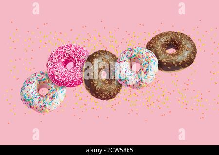 ciambelle smaltate in movimento cadendo su sfondo rosa con colorato spruzzare Foto Stock