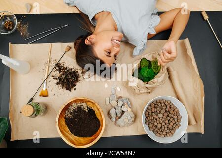 Donna felice che giace su un tappetino sul pavimento con articoli a tema di giardinaggio interno. Foto Stock