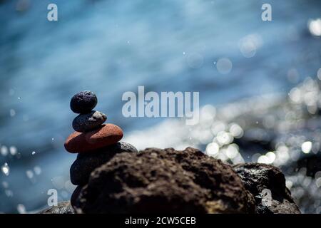 Colpo di closeup di ciottoli impilati l'uno sull'altro in un equilibrio con il mare blu sullo sfondo Foto Stock