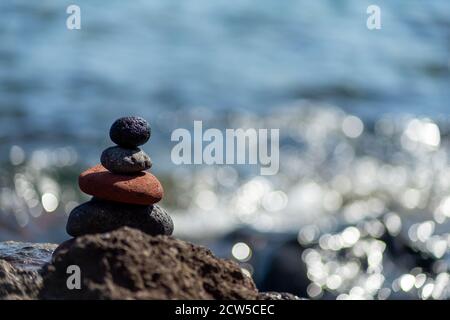 Colpo di closeup di ciottoli impilati l'uno sull'altro in un equilibrio con il mare blu sullo sfondo Foto Stock