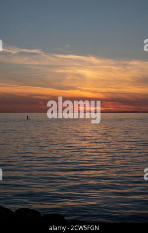 Un uomo in piedi su una tavola da surf sulla calma bay Water con la centrale nucleare Barsebäck visibile L'orizzonte durante l'estate in Svezia Foto Stock