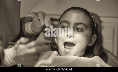 Giovane donna caucasica con dentista in guanti bianchi in lattice controllare le condizioni dei suoi denti. Bambina in sedia dentale blu Foto Stock