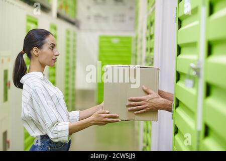 Vista laterale di una giovane donna che tiene una scatola di cartone e che si consegna all'uomo mentre si imballano unità di deposito auto, spazio di copia Foto Stock