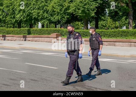 Due guardie del corpo armate in uniformi nere, maschere protettive, guanti pattugliano le strade della città durante la pandemia globale.sorveglianza dell'ordine urbano. Foto Stock