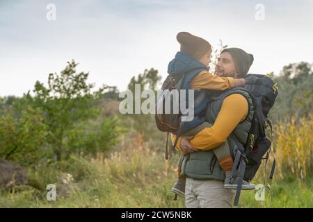 Giovane padre affettuoso con zaino holdng suo figlio carino sulle mani Foto Stock