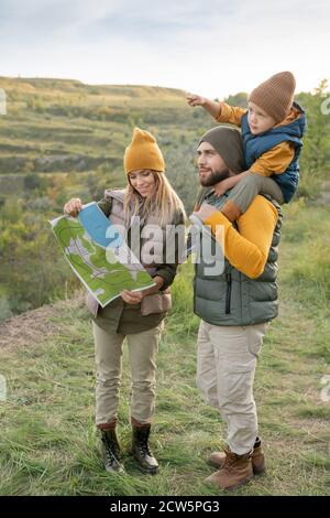 Giovane famiglia di backpackers che guarda la mappa, mentre piccolo ragazzo rivolto in avanti Foto Stock