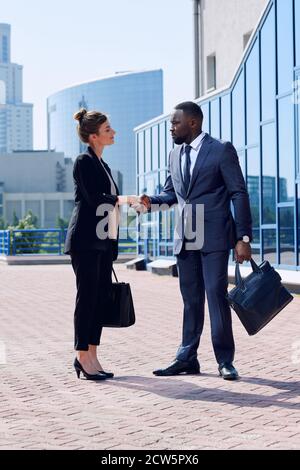 Giovani partner commerciali interculturali di successo in abbigliamento da formalwear che scuotono le mani Foto Stock