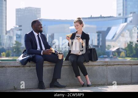 Due giovani e felici partner commerciali interculturali in abbigliamento da formalwear che pranzano Foto Stock
