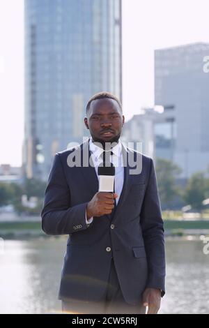 Felice giovane ed elegante reporter di etnia africana che parla al microfono Foto Stock