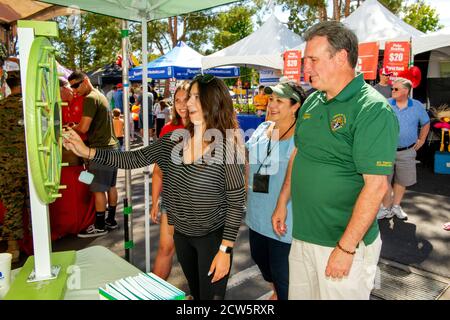 Un diacono cattolico socializza con i giovani parrocchiani a ruota d'azzardo durante una mostra itinerante di Street fair a Laguna Niguel, CA. Foto Stock