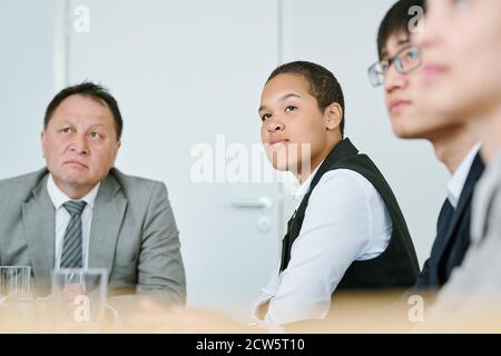 Giovane donna d'affari mista seria in abbigliamento da formalwear ascoltando allenatore Foto Stock