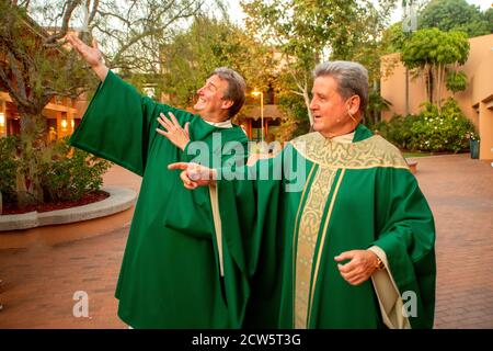 Indossando abiti cerimoniali verdi, un diacono e un monsignor colpiscono una posa umorosa nel cortile di una chiesa cattolica della California meridionale. Foto Stock