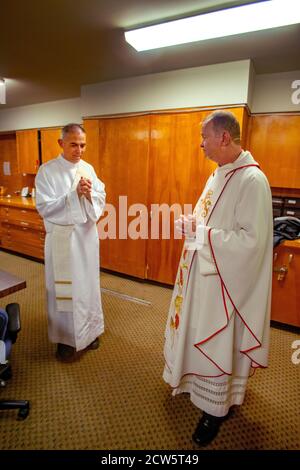 Indossando abiti cerimoniali, un sacerdote e il suo diacono si conferiscono mentre si prepara alla messa in una chiesa cattolica della California meridionale. Foto Stock