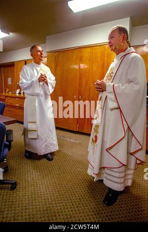 Indossando abiti cerimoniali, un sacerdote e il suo diacono si conferiscono mentre si prepara alla messa in una chiesa cattolica della California meridionale. Foto Stock