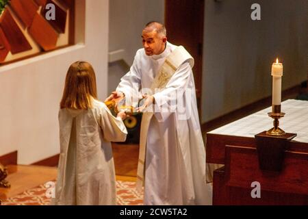 Un diacono a rondine riceve ciotole di acqua Santa da un assistente femminile mentre partecipa alla messa presso l'altare di una chiesa cattolica della California meridionale. Foto Stock