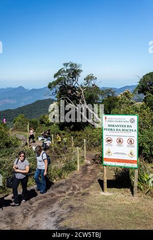 I turisti provenienti dal punto di osservazione inferiore di Pedra da Macela punto di riferimento dal sentiero sterrato recintato da corde, vicino a un cartello informativo. Foto Stock