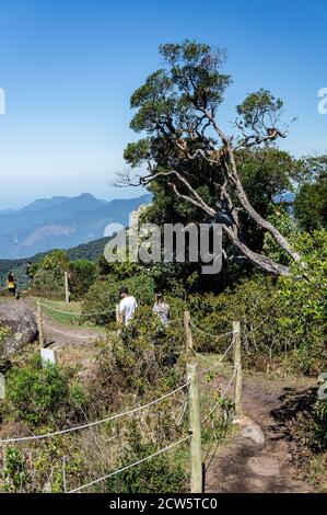 I turisti camminano verso il punto di osservazione inferiore di Pedra da Macela punto di riferimento dal sentiero sterrato recintato da corde, vicino ad un grande albero. Foto Stock