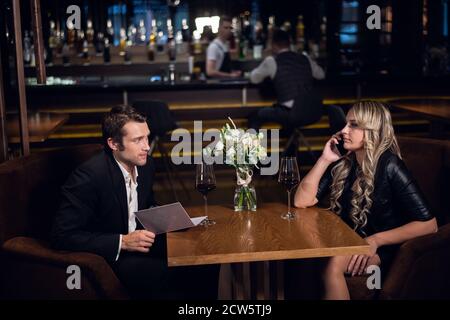 un giovane fa un ordine al bar, una bella ragazza parla al telefono al tavolo Foto Stock