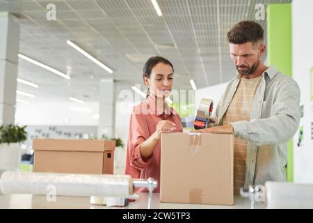 Vita ritratto di coppia moderna adulti imballaggio scatole di cartone con pistola a nastro in struttura di deposito o servizio di spedizione, copia spazio Foto Stock