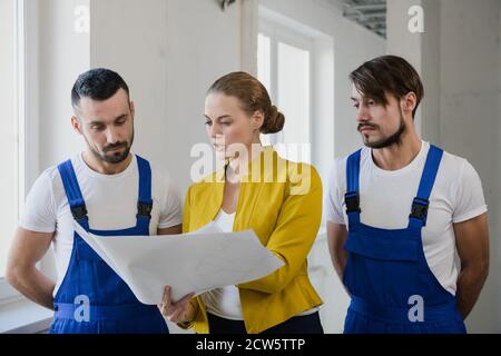Un brigadiere con un piano nelle sue mani sta parlando a due costruttori in tute Foto Stock
