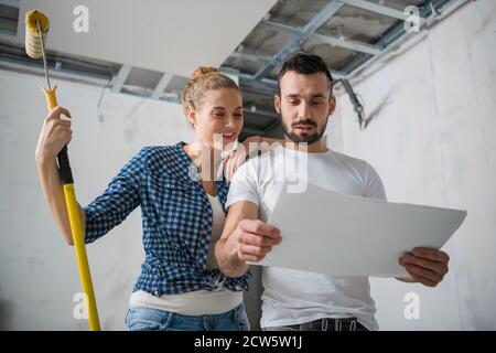 Una donna tiene un rullo in mano e abbraccia il suo ragazzo. Guardano alla disposizione degli appartamenti Foto Stock