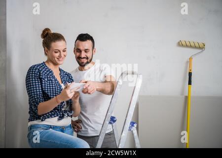 La donna e il suo ragazzo guarda le foto sullo schermo del telefono. Fanno una pausa dai lavori di ristrutturazione Foto Stock