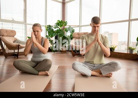 Giovane coppia meditante in abbigliamento sportivo seduto in posa di lotus sui tappetini Foto Stock