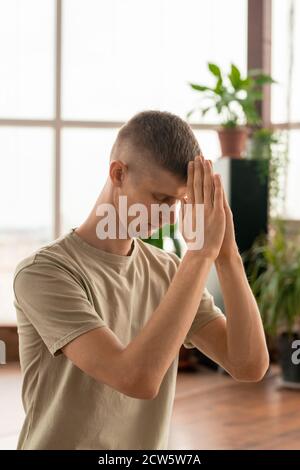 Giovane uomo con le mani unite davanti fronte tenendo gli occhi chiusi Foto Stock