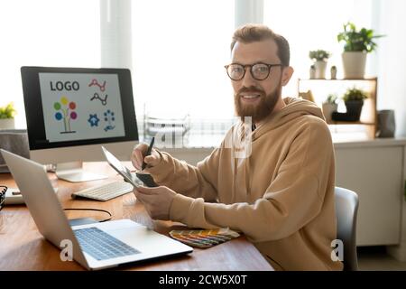 Giovane allegro e creativo uomo freelance designer disegno logo vicino luogo di lavoro Foto Stock