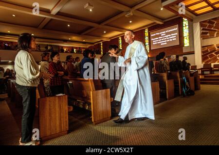 Un diacono amichevole accoglie un parishioner in arrivo a massa in una chiesa cattolica della California meridionale. Foto Stock