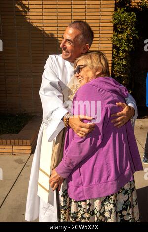 Dopo la messa, il diacono di una chiesa cattolica della California meridionale abbracca un parishioner nel cortile esterno della chiesa. Foto Stock