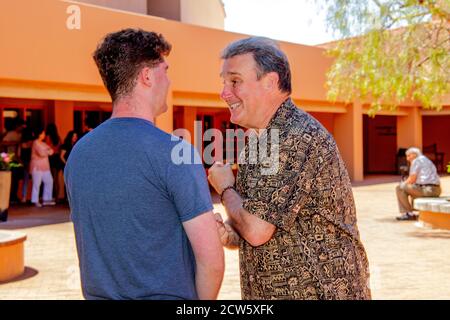 Il diacono di una chiesa cattolica della California meridionale accoglie un giovane parishioner adulto dopo la messa nel cortile della chiesa. Foto Stock