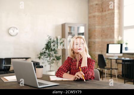 Pensiva donna d'affari bionda matura seduta di fronte al portatile e. contemplare Foto Stock