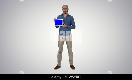 Uomo arabo che mostra uno schermo del tablet vuoto su sfondo sfumato. Foto Stock