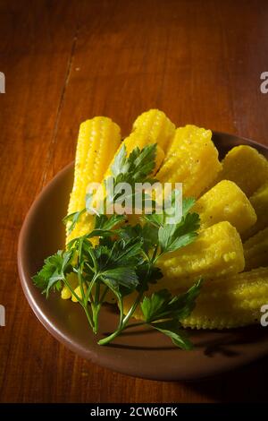 Piccole pannocchie di mais in un piatto su un tavolo di legno Foto Stock