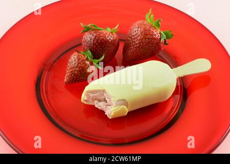 Barra gelato alla fragola immersa in cioccolato bianco belga con fragole su vetro rosso su sfondo rosa Foto Stock