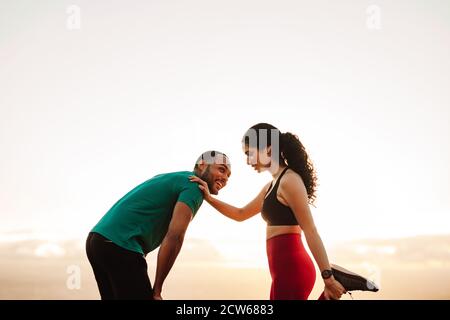 Uomo e donna atletici in piedi all'aperto rilassandosi dopo l'allenamento. Coppia allegra di fitness che si allenano in piedi all'aperto. Foto Stock