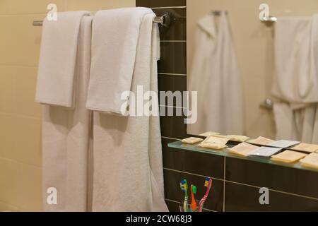 Fotografia dei moderni interni del bagno dell'hotel. Due asciugamani bianchi appesi. Pulire lo specchio. Confezioni monouso di shampoo e gel doccia. Dente Foto Stock