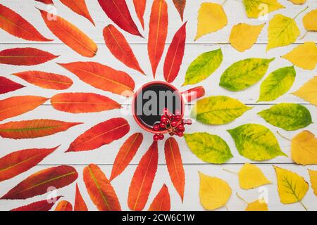 Tazza di tè rosso con bacche di viburno e foglie di autunno gialle su un tavolo di legno, composizione piatta autunnale, astrazione creativa colorata, cartellino stagionale Foto Stock