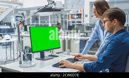 Tecnico che parla con Project Manager e lavora con il computer desktop Green Mock-up Screen. Nello stabilimento di ingegneria di background specializzato su Foto Stock