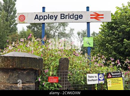 Il segnale della stazione si trova a Appley Bridge in una mattinata bagnata a Greater Manchester. Le indicazioni includono ancora il vecchio simbolo della doppia freccia della British Railways. Foto Stock