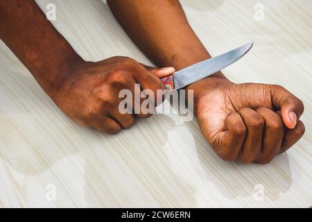 Suicidio commesso concetto - l'uomo vuole suicidarsi tagliando le vene con coltello in isolato sullo sfondo pavimento. Uomo suicidio da coltello taglio a Foto Stock