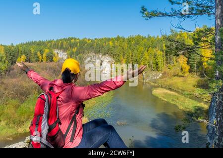 Paesaggio con vista sul fiume e la foresta d'autunno dalla cima della scogliera. Una ragazza a braccia aperte si siede sulla cima e gode l'escursione, Ural, Ekat Foto Stock