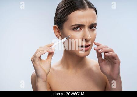 Bella donna che si sente confuso durante l'iniezione del viso Foto Stock