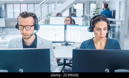 Nel moderno ufficio open space: Team di addetti all'assistenza clienti e venditori che lavorano sui computer desktop, utilizzando cuffie e effettuando chiamate Foto Stock