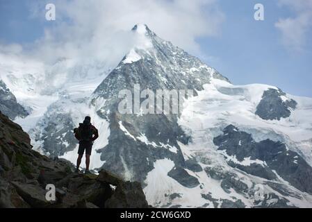 Immagine orizzontale del turista maschile, in piedi con la schiena alla macchina fotografica e godendo la bellezza del monte Ober Gabelhorn nelle Alpi svizzere. Concetto di viaggio, turismo, escursionismo e alpinismo Foto Stock