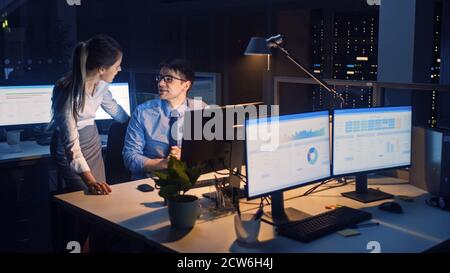 Di notte in ufficio moderno: Il lavoratore di ufficio seduto e lavorando al suo computer desktop, discute Problem Solution WIT Project Manager, che guardano Foto Stock