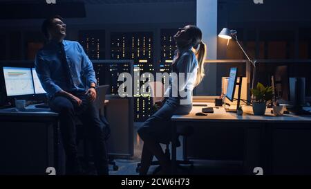A tarda notte nell'ufficio corporativo due giovani professionisti che chiacchierano amichevoli, scambiano le notizie, parlano del lavoro, Flirting Foto Stock